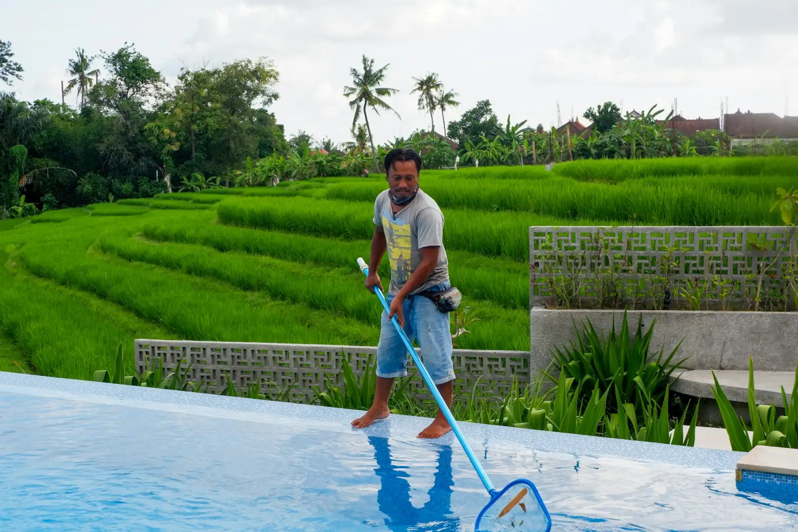 A pool technician cleaning a swimming pool with a long pole
