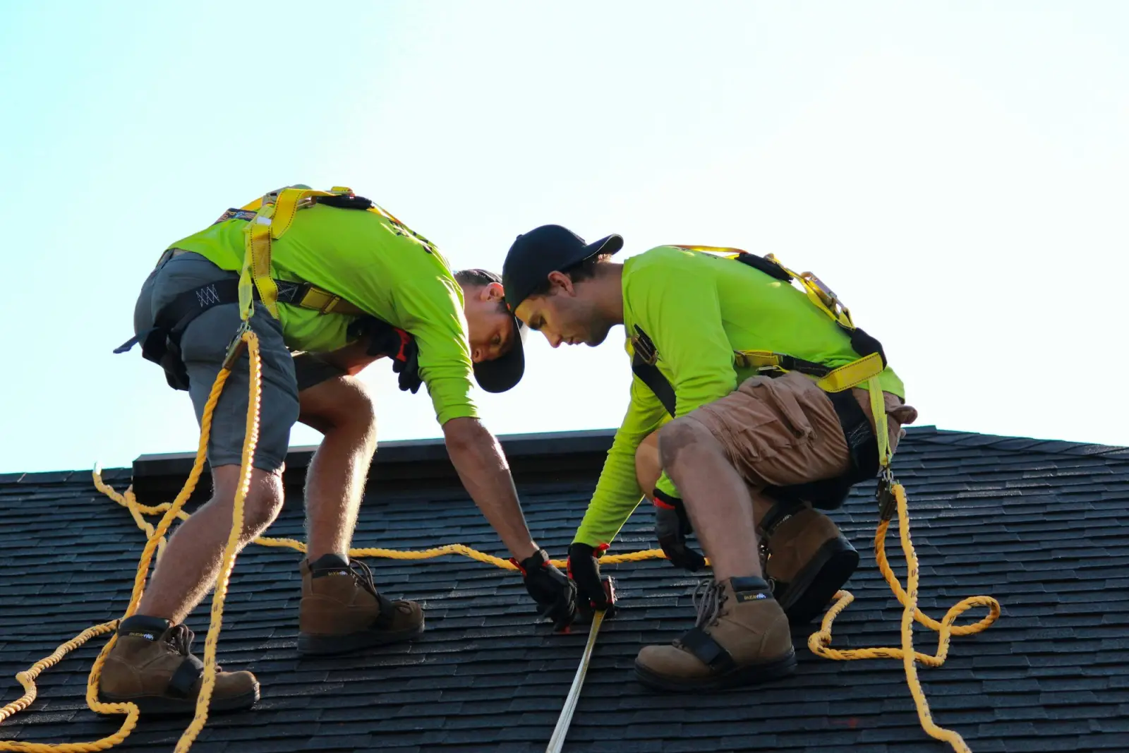 Two roofers in high-visibility shirts working on a shingle roof